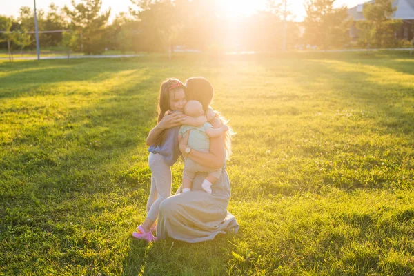 Vacker kvinna med dotter och baby son på grönt gräs fält. Mamma med två små barn kramas utomhus. Lycklig familj koncept — Stockfoto