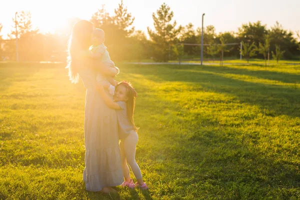 Красива жінка з дочкою і маленьким сином на зеленому трав'яному полі. Мама з двома маленькими дітьми обіймається на відкритому повітрі. Щаслива сімейна концепція — стокове фото