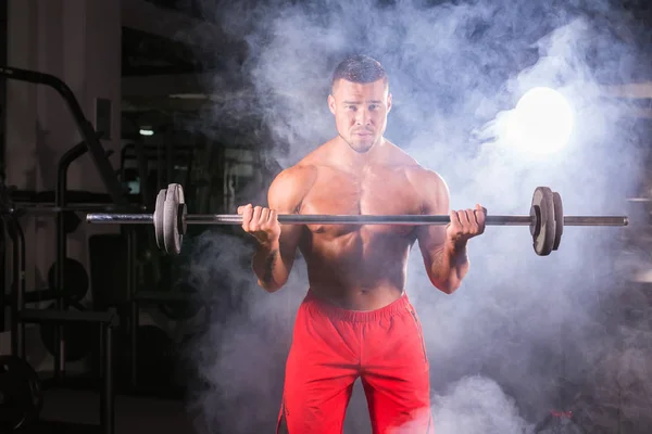 Bodybuilder, der die Übungen mit der Langhantel macht. kräftiges Männchen mit nacktem Oberkörper auf dunklem Hintergrund. Stärke und Motivation. — Stockfoto