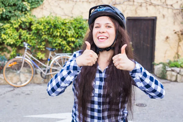 헬멧과 선글라스 배경 골목 및 자전거에 엄지를 나타나고 젊은 여자 — 스톡 사진