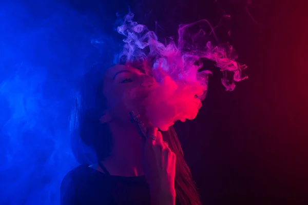 Молодая женщина курит vape или электронную сигарету в неоновом свете — стоковое фото