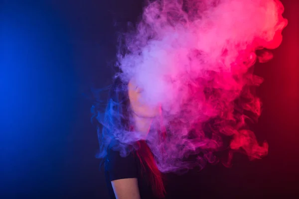 Jovem mulher em t-shirt preta vaping em luz de néon vermelho e azul — Fotografia de Stock