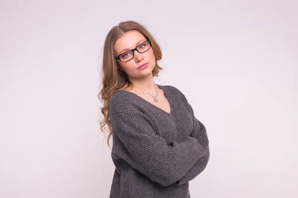 Emotionen und Menschen-Konzept - junge Frau auf weißem Hintergrund in grauem Strickpullover, die sich umarmt und in die Kamera blickt — Stockfoto