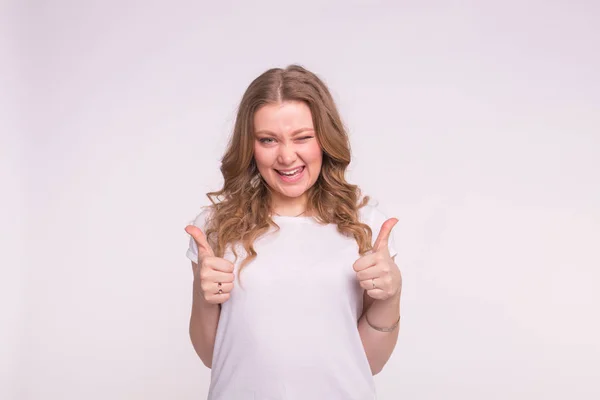 Concepto de moda, estilo y gesto: mujer bonita guiñando un ojo sobre fondo blanco que muestra los pulgares hacia arriba sobre fondo blanco — Foto de Stock