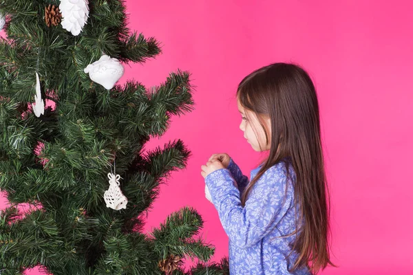Little girl decorating christmas tree on pink background — Stock Photo, Image
