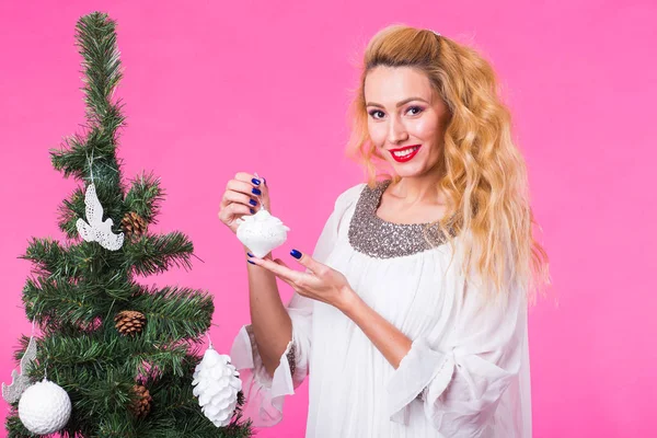Άνθρωποι, τις διακοπές και τα Χριστούγεννα έννοια - νεαρός ξανθιά γυναίκα διακόσμηση του Χριστουγεννιάτικου δέντρου σε ροζ φόντο — Φωτογραφία Αρχείου