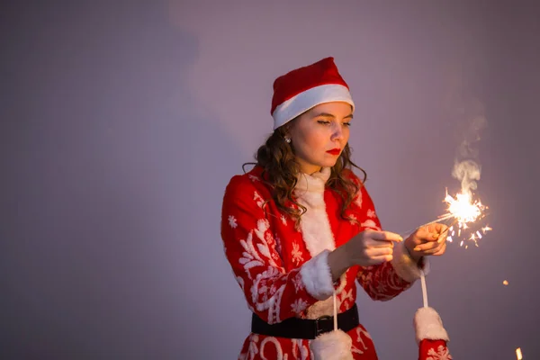 Lächelnde Weihnachtsfrau in Weihnachtsmütze mit Wunderkerze und Bengalfeuer im Hintergrund — Stockfoto