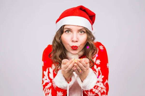 Menschen, Weihnachts- und Feiertagskonzept - hübsche junge Dame im Weihnachtsmann-Kostüm pustet Konfetti auf weißem Hintergrund — Stockfoto