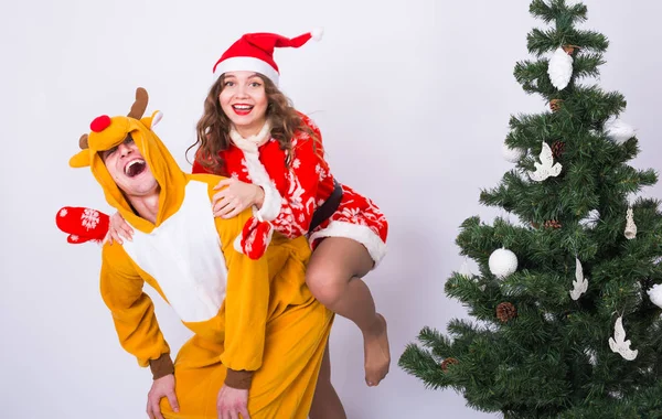 Femme et homme souriants en costumes de carnaval de cerf et Père Noël sur fond clair avec arbre de Noël — Photo