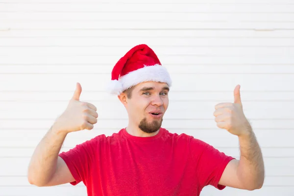 Mladý muž s vánoční čepice, takže palec nahoru znamení na bílém pozadí — Stock fotografie