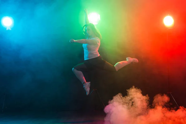 Baile, deporte, jazz funk y el concepto de la gente - mujer joven saltar en la oscuridad bajo una luz colorida — Foto de Stock