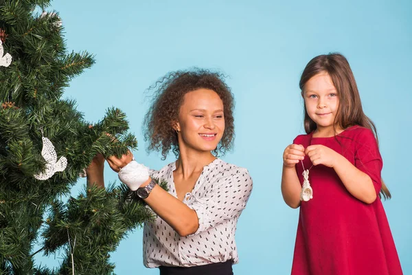 Helgdagar, familj och jul koncept - blandad ras mor och dotter dekorera julgran på blå bakgrund — Stockfoto