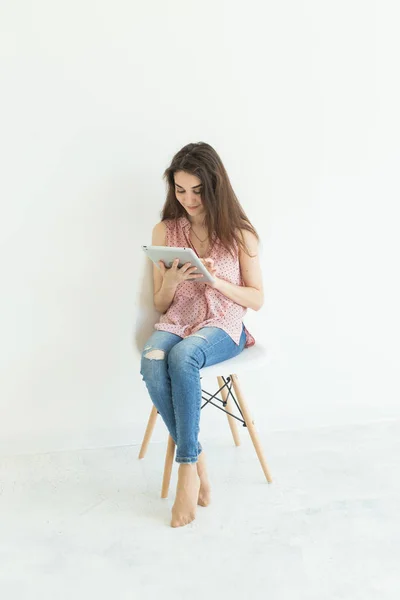 Jovem mulher sentada na cadeira e assistindo tablet digital ou navegar na Internet em fundo branco — Fotografia de Stock