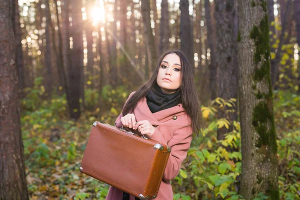 Mujer joven y elegante con maleta retro caminando en el parque de otoño — Foto de Stock