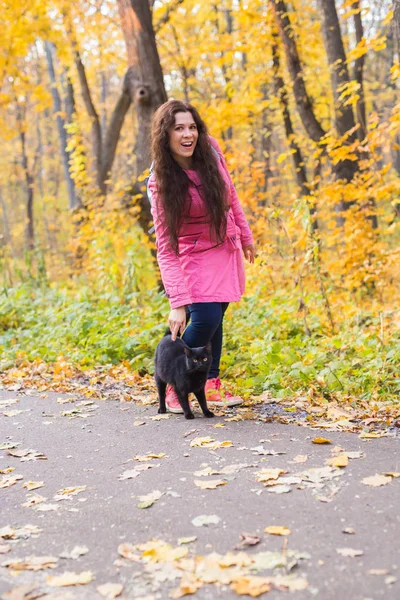 Haustiere und Menschen - junge Frau streichelt die schwarze Katze im Herbstpark — Stockfoto