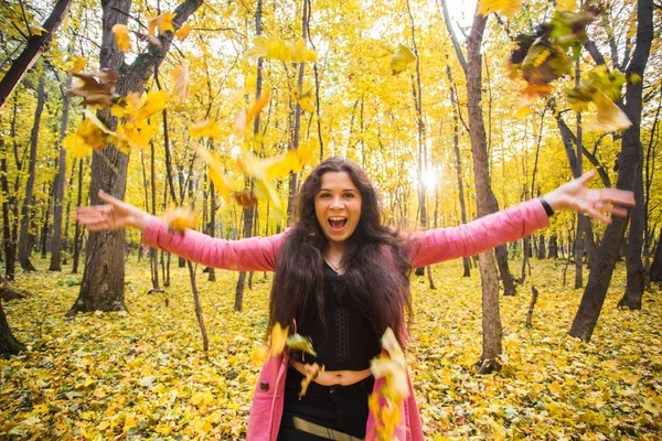 Осінь, щастя, концепція людей - молода жінка розважається в осінньому парку. Вона кидає жовте листя в небо — стокове фото
