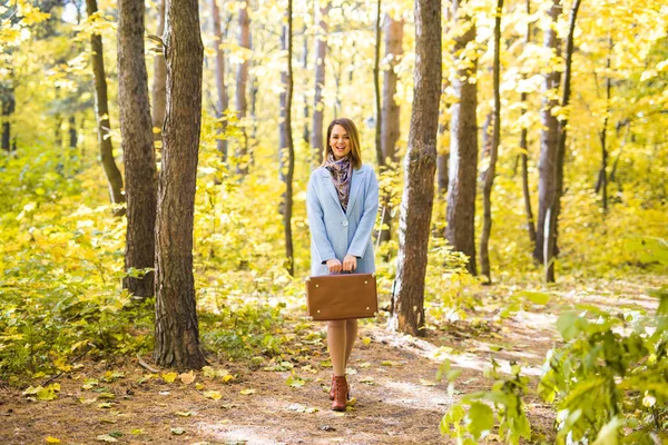 Outono, moda, conceito de pessoas - mulher com mala retro marrom andando pelo parque de outono e sorrindo — Fotografia de Stock