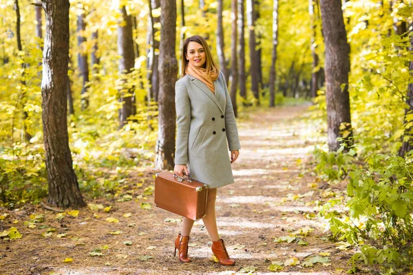 Jovem mulher elegante com mala retro andando no parque de outono — Fotografia de Stock