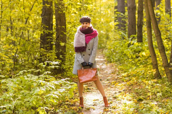 Autumn, season and people concept - woman in coat with brown bag standing in autumn park — Stock Photo, Image