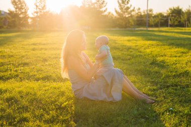 Güneşli bir çayır çocuğu olan kadın. Yaz günbatımı üzerinde mutlu bir aile. Bebek annesiyle.