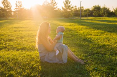 Güneşli bir çayır çocuğu olan kadın. Yaz günbatımı üzerinde mutlu bir aile. Bebek annesiyle.