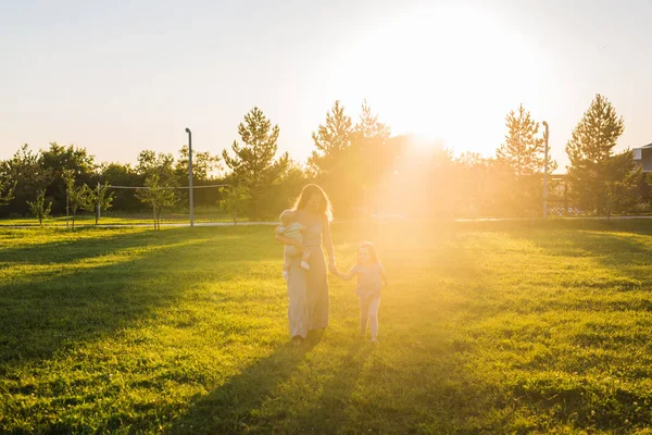 Vacker kvinna med dotter och baby son på grönt gräs fält. Mamma med två små barn gå utomhus. Lycklig familj koncept — Stockfoto