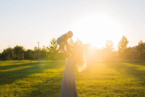 Jovem com rapaz no prado num dia ensolarado. Família feliz no pôr-do-sol de verão. Mãe com bebê . — Fotografia de Stock