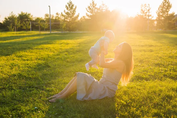Jovem com rapaz no prado num dia ensolarado. Família feliz no pôr-do-sol de verão. Mãe com bebê . — Fotografia de Stock