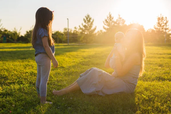 Mujer joven con hijo e hija en el prado en un día soleado. Familia feliz en el atardecer de verano. Madre con bebé . —  Fotos de Stock