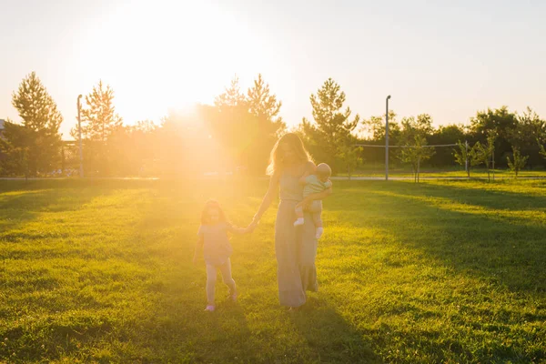 Mulher bonita com filha e filho bebê no campo de grama verde. Mãe com duas crianças pequenas andando ao ar livre. Conceito de família feliz — Fotografia de Stock