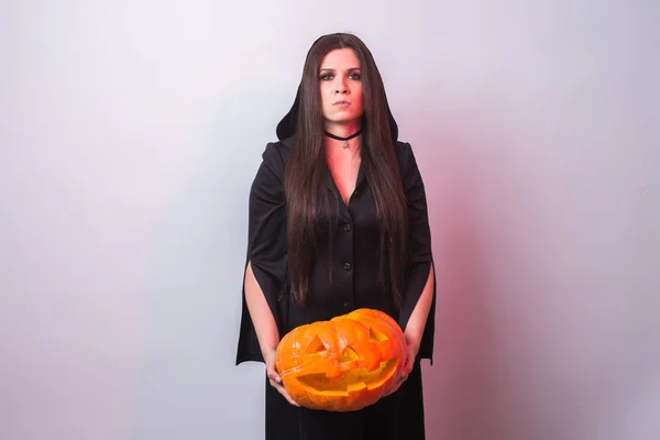 Gothic young woman in witch halloween costume with a carved pumpkin on white background with copy space — Stock Photo, Image