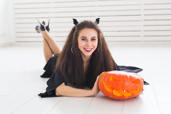 Aufgeregte, fröhliche junge Frau im Halloween-Kostüm posiert mit geschnitztem Kürbis im Lichtersaal — Stockfoto