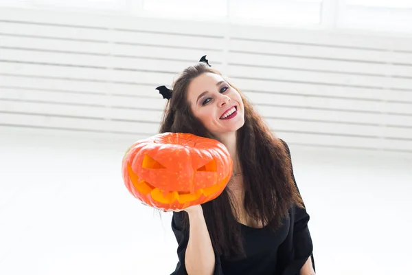 Opgewonden gelukkig jonge vrouw in halloween kostuum poseren met gebeeldhouwde pompoen in lightroom — Stockfoto