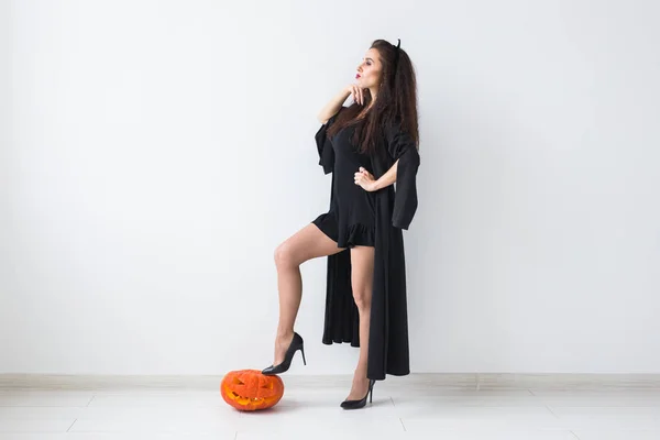Smiling brunette woman in halloween makeup posing with carved pumpkin over light background with copy space — Stock Photo, Image