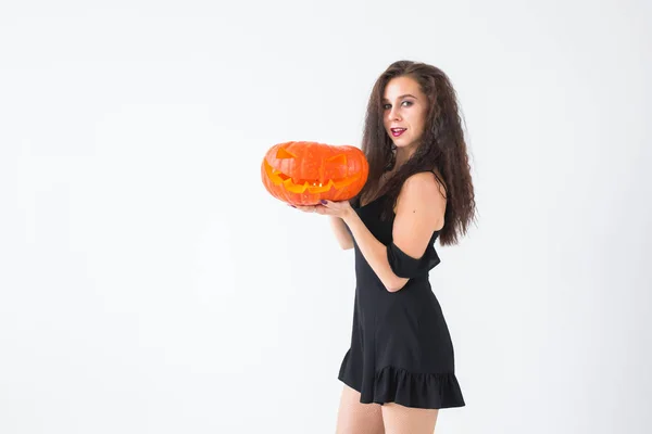 Jeune femme heureuse excitée en costume d'Halloween posant avec citrouille sculptée sur fond clair avec espace de copie — Photo