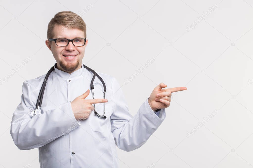 Portrait of happy young doctor in studio with stethoscope pointing left