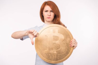 Büyük bir altın bitcoin tutarak ve başparmak aşağı gösterilen mutsuz Kızıl saçlı kadın