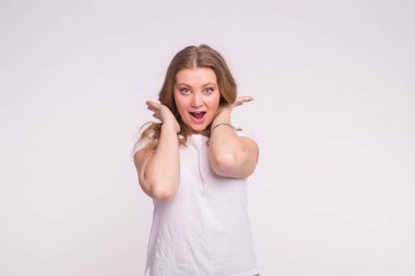 Kıvırcık sarı saçlı beyaz arka plan üzerinde merak ve beyaz t-shirt giyen mutlu beyaz genç kadın portresi