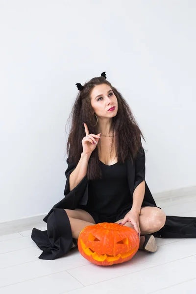 Opgewonden gelukkig jonge vrouw in halloween kostuum poseren met gebeeldhouwde pompoen in lightroom — Stockfoto