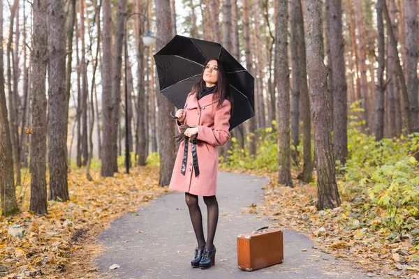 Estação, natureza e conceito de pessoas - Mulher no parque de outono andando com mala retro e guarda-chuva — Fotografia de Stock
