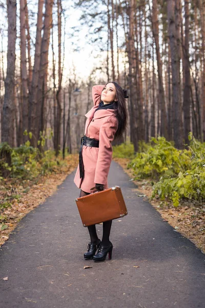 Mode-, seizoen- en mensen-concept - gelukkige jonge vrouw gaat reis met retro koffer op een achtergrond van de herfst bladeren — Stockfoto