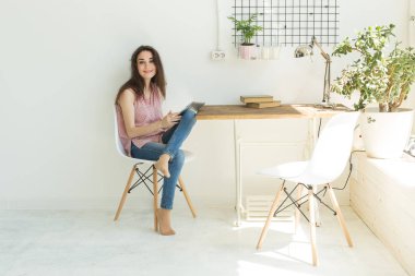 Teknoloji ve insan kavramı - dijital tablet ile beyaz masada oturan genç güzel kadın