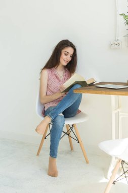 Okuma, eğitim, kültür, insanlar kavramı - genç bir beyaz odada beyaz sandalyede oturuyor iken öğrenci kadın bir kitap okuyor