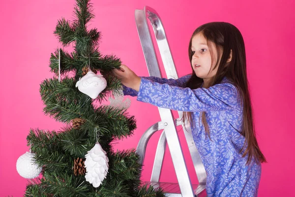 Children, holidays and christmas concept - little girl decorating christmas tree on pink background — Stock Photo, Image