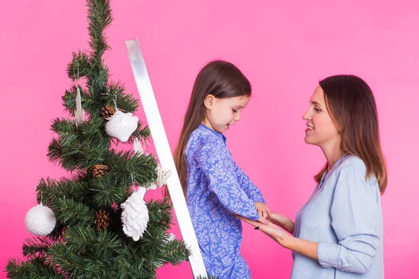 Wakacje, rodzinne i świąteczne koncepcja - Ładna dziewczyna z mamą są dekorowanie choinki na różowym tle — Zdjęcie stockowe
