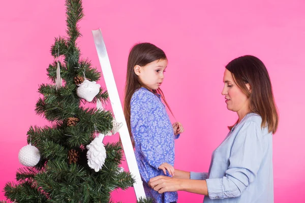 Ung mamma och hennes dotter med julgran på rosa bakgrund — Stockfoto