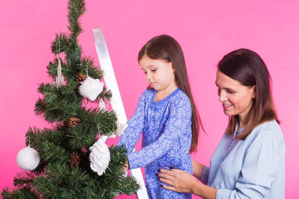 Helgdagar, familj och jul koncept - mor och dotter dekorera julgran på rosa bakgrund — Stockfoto