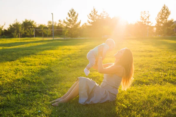 Ung kvinna med pojke på ängen på en solig dag. Lycklig familj på sommar solnedgång. Mor med baby. — Stockfoto