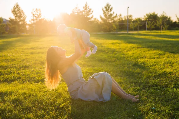 Jeune femme avec garçon dans la prairie par une journée ensoleillée. Bonne famille au coucher du soleil d'été. Mère avec bébé . — Photo