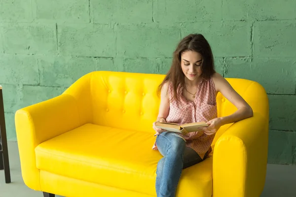 사람, 교육 및 인테리어 개념-젊은 여자는 소파에 앉아서 책을 읽고 — 스톡 사진